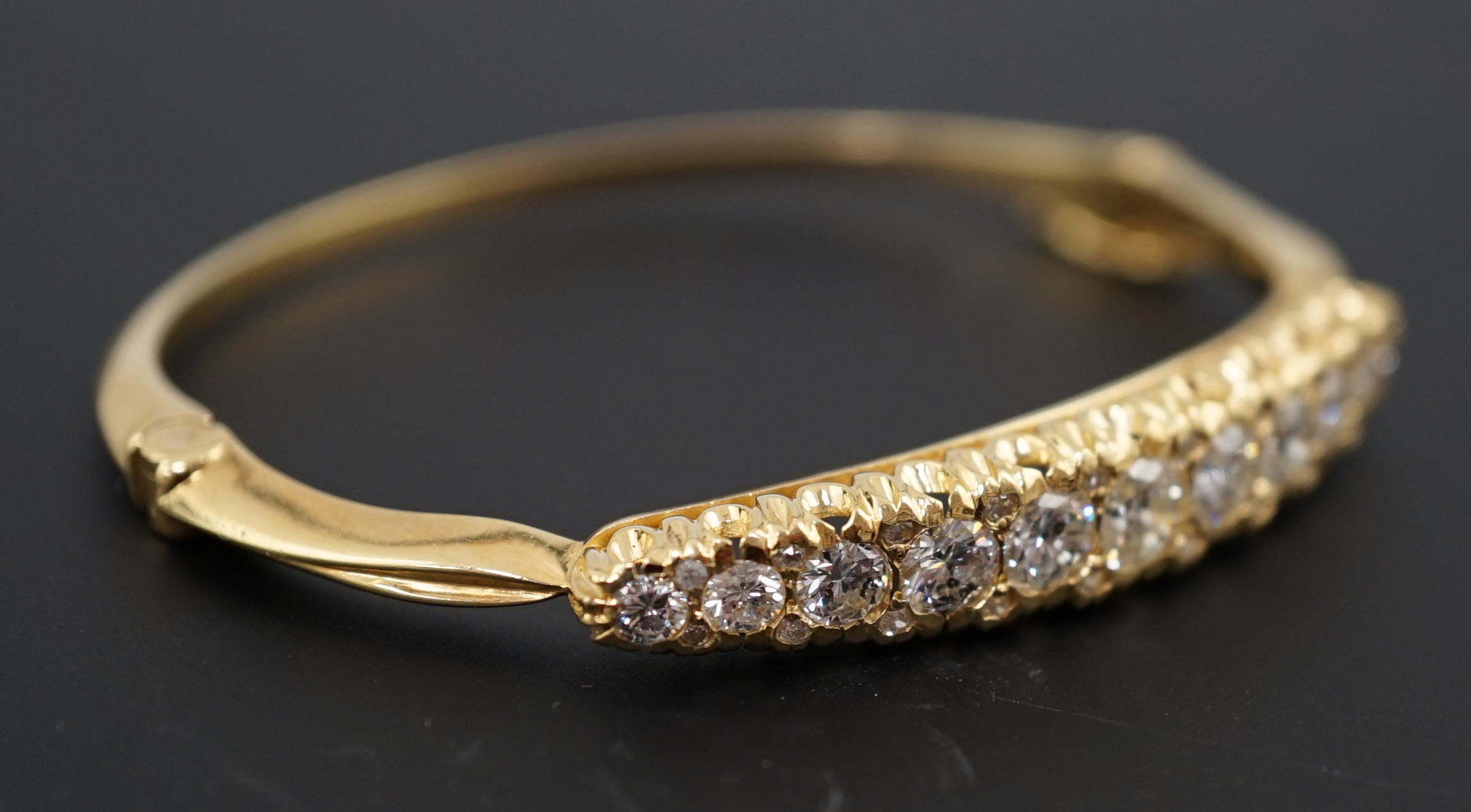 A gold and graduated eleven stone diamond set hinged bangle